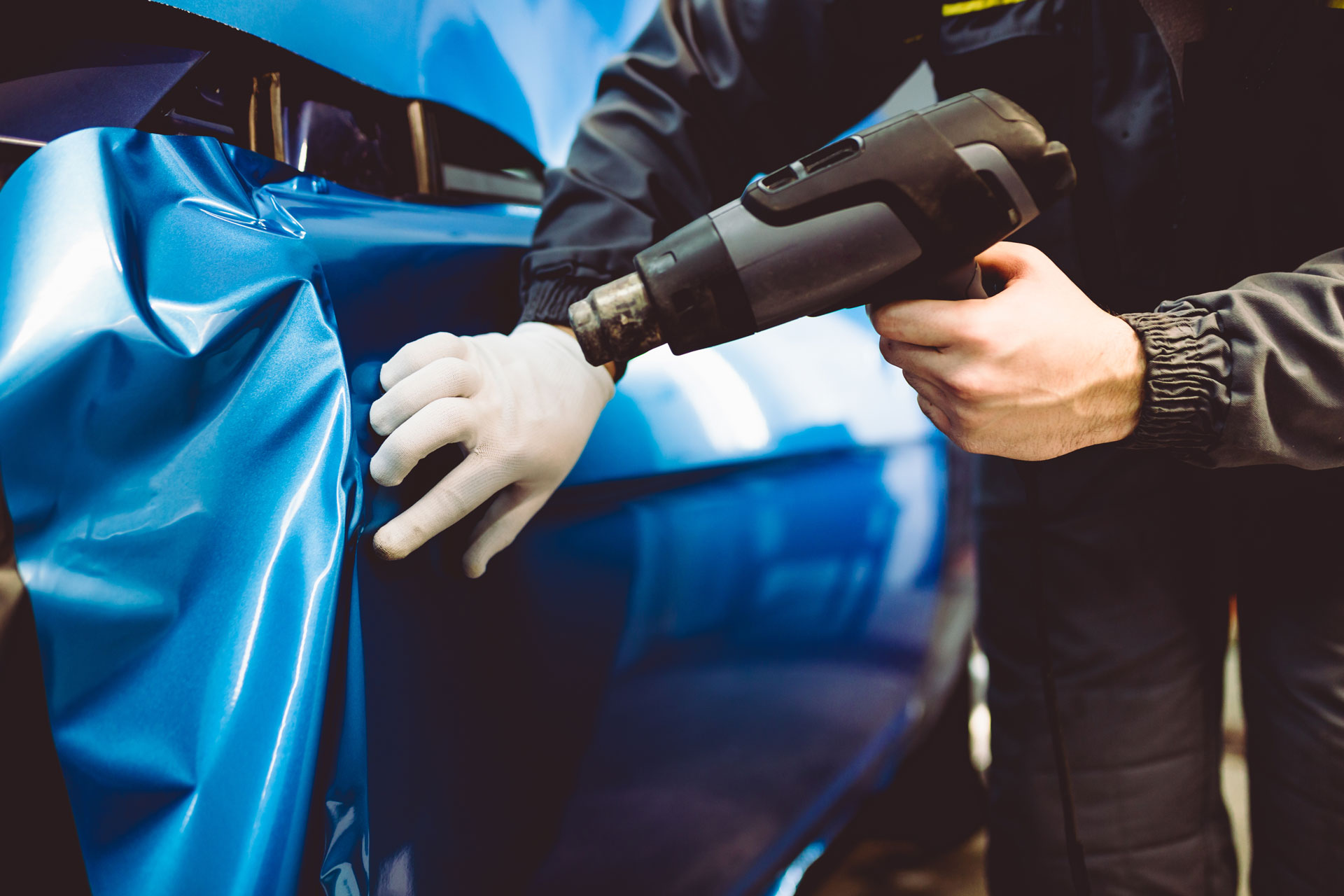 Person applying a matte vinyl wrap to a car door using a squeegee tool in an auto workshop