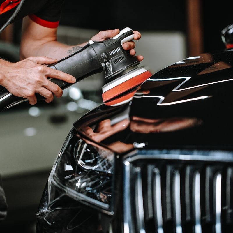 Person using a polishing machine to buff and shine the hood of a black car